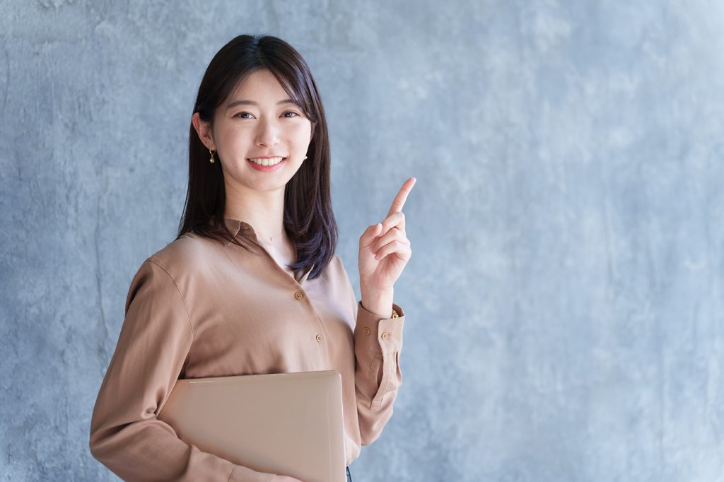 ノートPCを持って人差し指を立ててポイント解説している女性